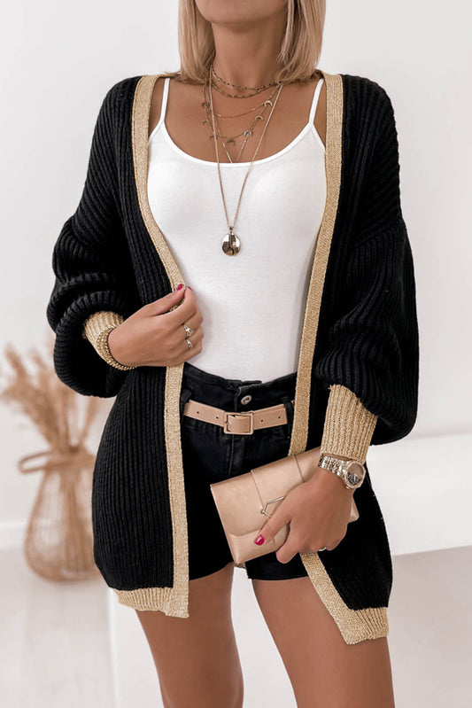 Fashionable black cardigan with contrast trim, lantern sleeves, and open front, styled with a white top and chic accessories.